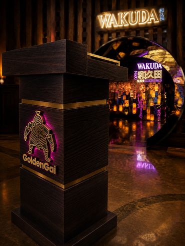 Wooden podium with GoldenGai logo and WAKUDA neon signs.