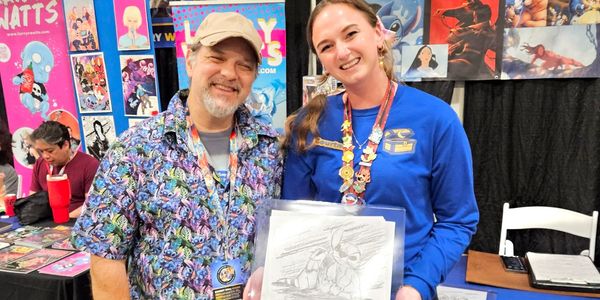 Two smiling people at a convention booth holding an artwork sketch.