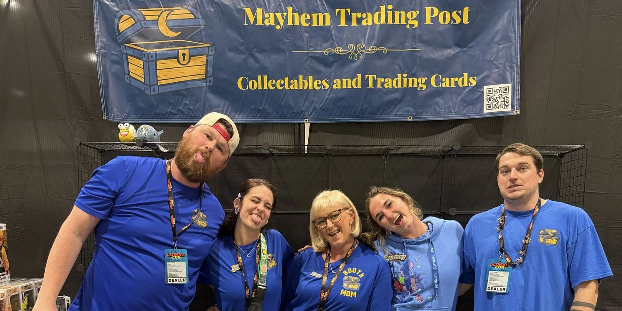 Five cheerful people posing at a trading cards booth.