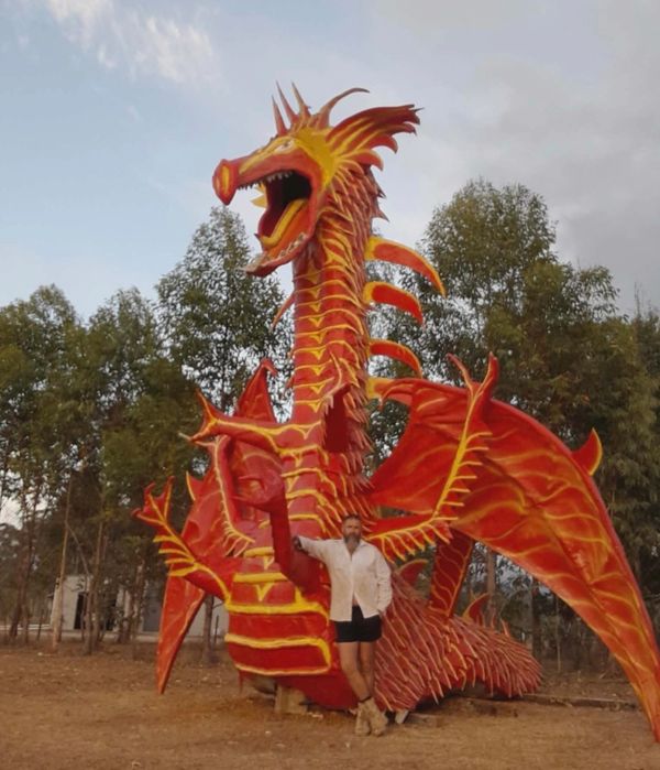 Person standing next to a large, vibrant red and yellow dragon sculpture outdoors.