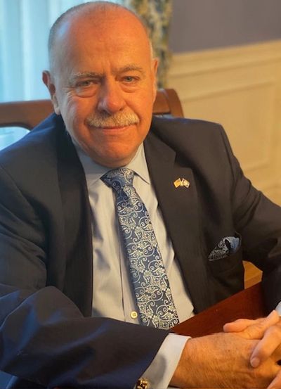 Smiling man in suit with patterned tie sitting at a wooden table.