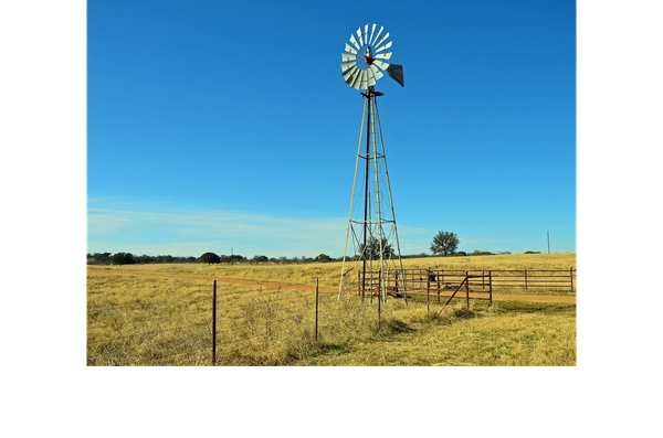 Windmill in a rural field under a clear blue sky.