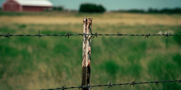 Rusty barbed wire fence post in a rural field.