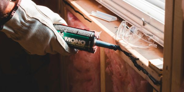 Applying black sealant around a window frame in construction.