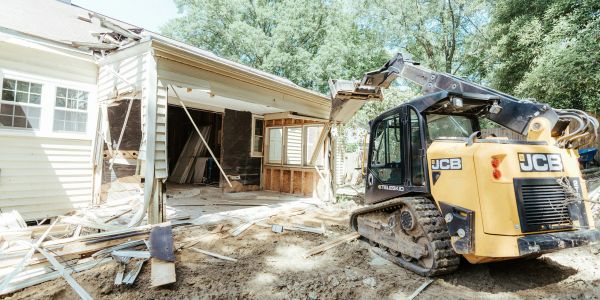 Tractor demolishes part of a house's exterior.
