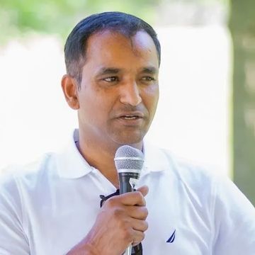 Man in white shirt speaking into a microphone outdoors.