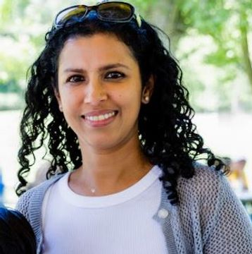 A smiling woman with curly black hair wearing sunglasses on her head.