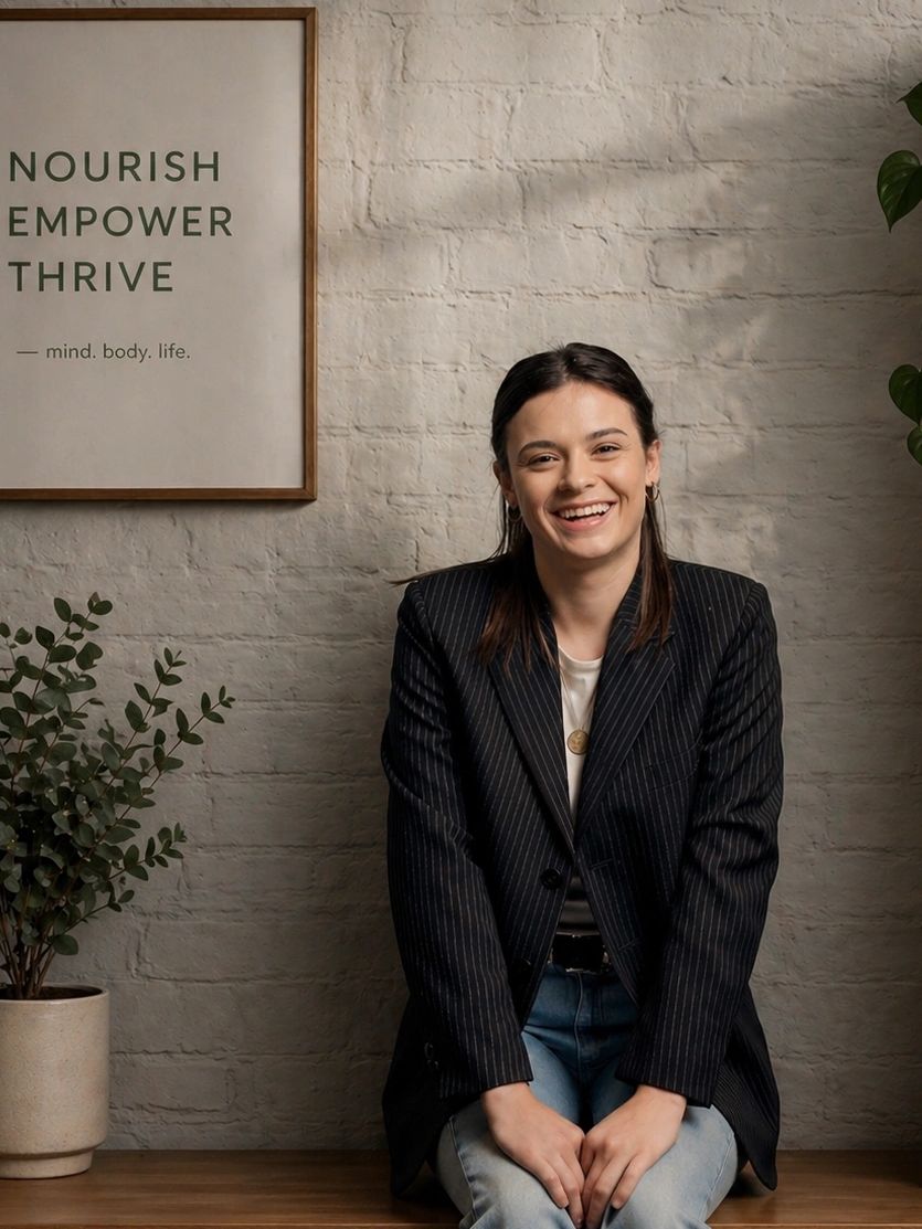 Smiling woman sitting indoors near a motivational poster and plant.