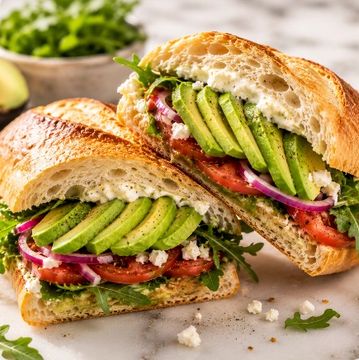 Avocado sandwich with tomato, onion, and cheese on ciabatta bread.