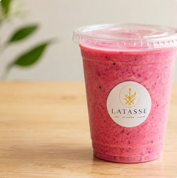 A pink smoothie in a plastic cup with a lid.