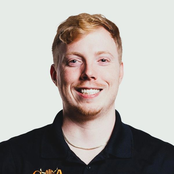 Smiling young man with red hair in a black polo shirt against a plain background.