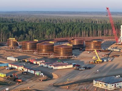 Industrial storage tanks under construction at a site near a forest.