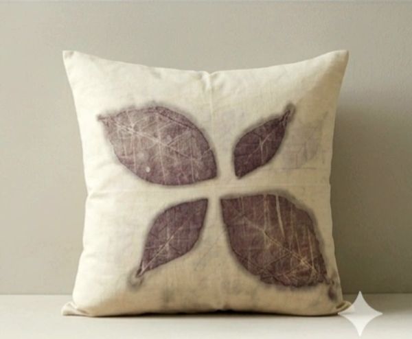 Decorative beige pillow with four brown leaf imprints arranged in a cross pattern.
