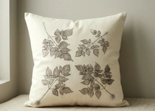 Cream pillow with four embroidered leaf patterns in grey.
