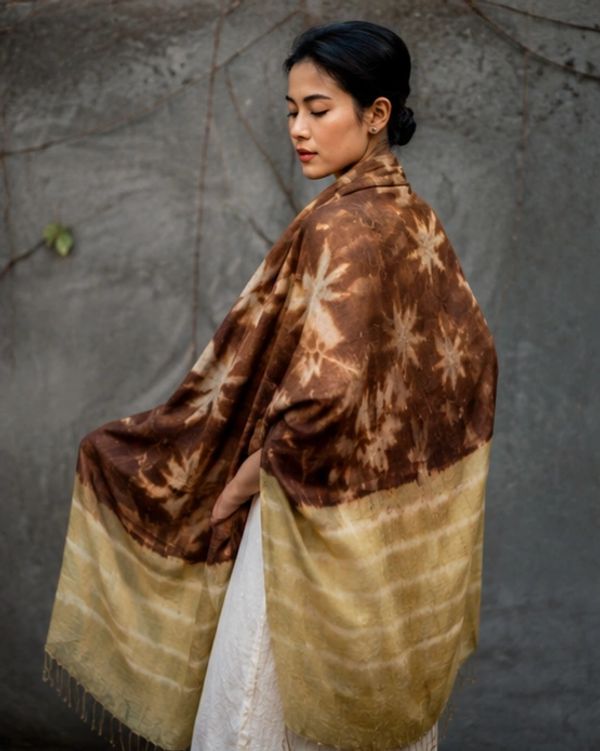 Woman wrapped in a brown and beige patterned shawl against a gray wall.