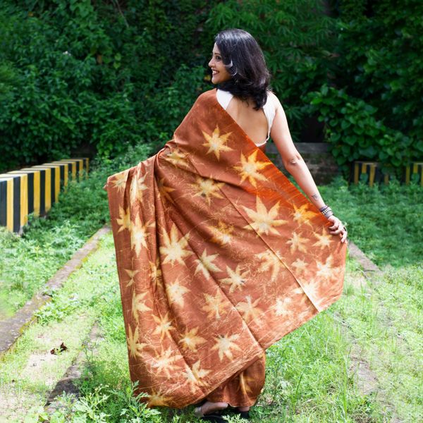 Woman smiling outdoors wearing a star-patterned brown saree.