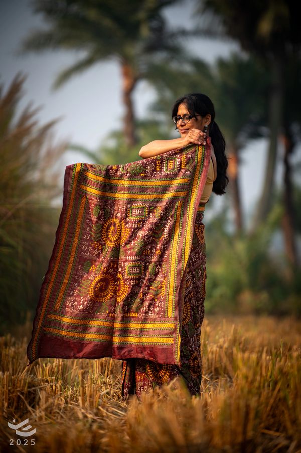 Woman holding a colorful traditional cloth in a field with palm trees.