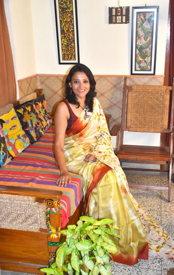 Woman in a yellow and orange saree sitting on a colorful couch indoors.