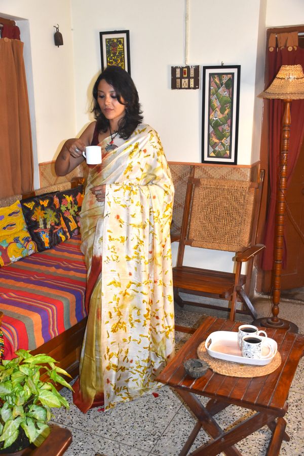 Woman in a floral saree enjoying a cup of tea in a cozy living room.