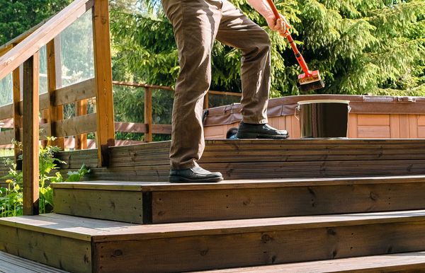 Person staining wooden deck steps outdoors.