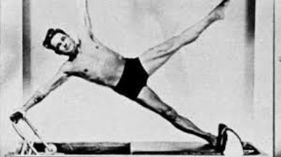 Man performing a side split on gymnastics rings in black shorts.