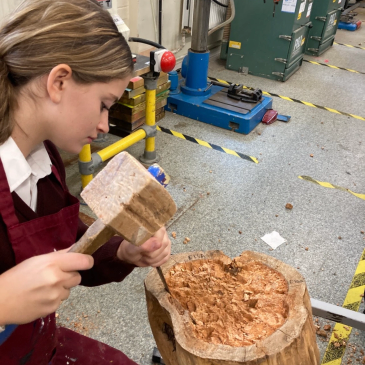 Young woman chiseling a large wooden log.