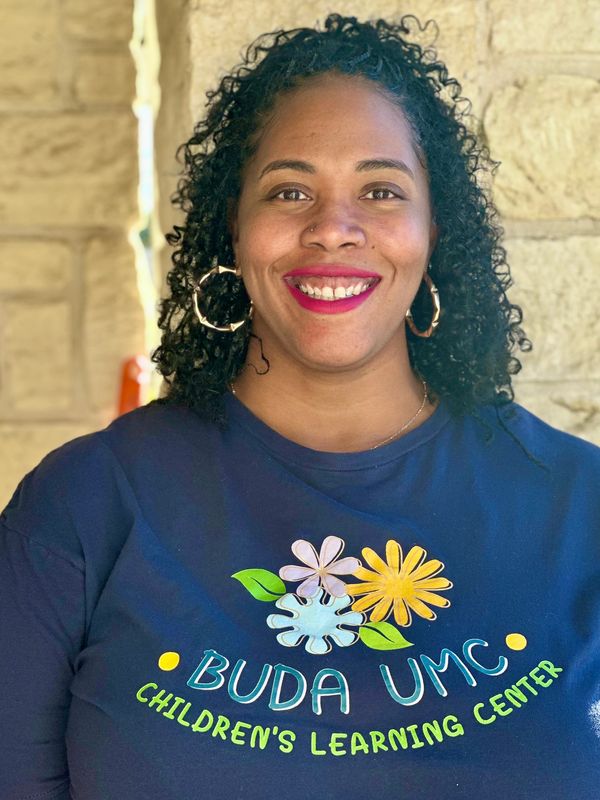 Woman smiling, wearing a Buda UMC Children's Learning Center shirt.