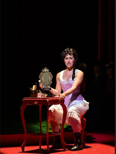 Woman in vintage dress sitting at a vanity table on stage.