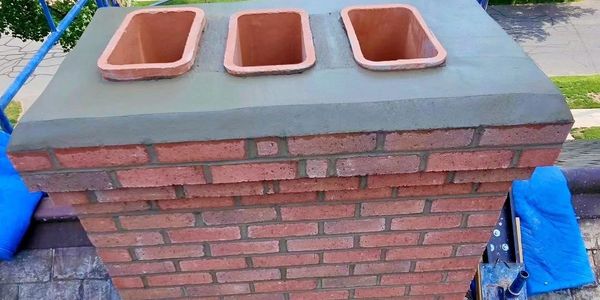 Newly constructed brick chimney with three flue liners on a rooftop scaffold.