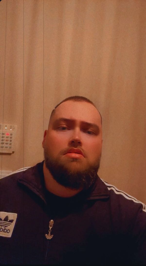 Man with a beard wearing an Adidas jacket, looking serious indoors.