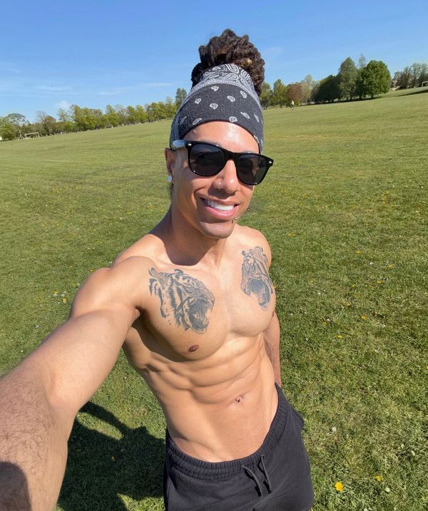 Shirtless man wearing sunglasses and headband posing outdoors.