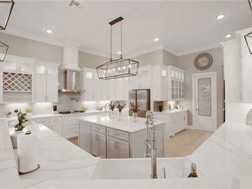 Bright, modern kitchen with white cabinetry and a large island under geometric pendant lights.