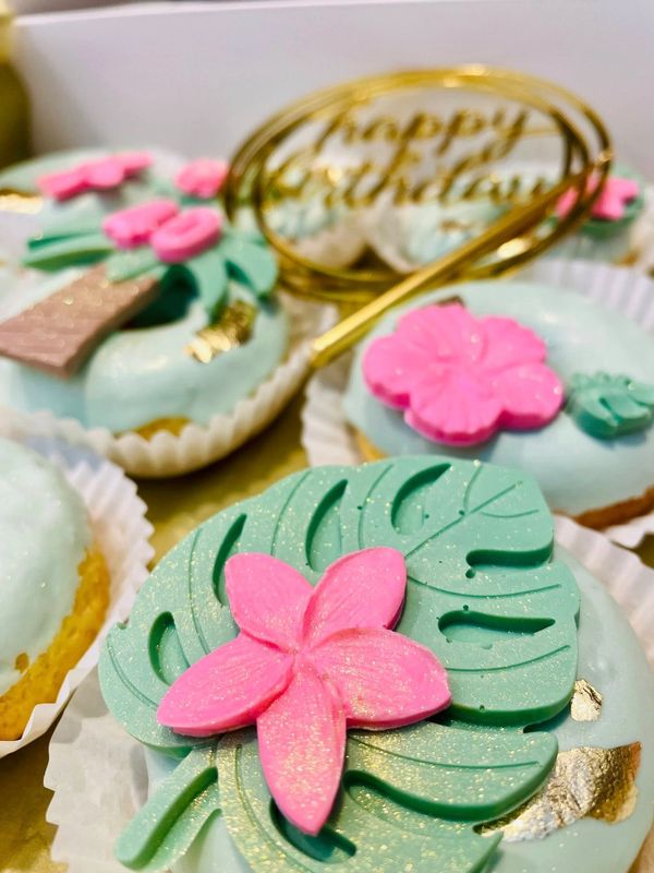 Decorated cupcakes with tropical leaves and pink flowers for a birthday.