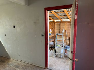Room under renovation with an open door leading to a cluttered workspace.