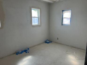 Empty room with patched walls and covered windows under renovation.