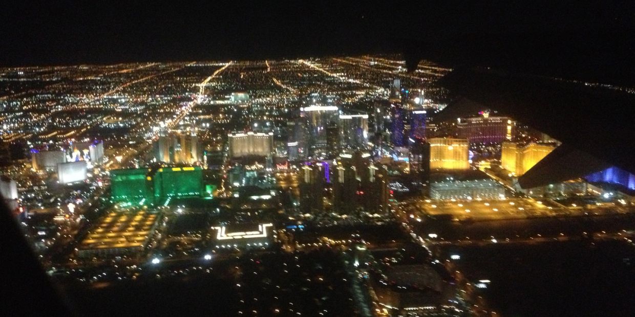 Aerial nighttime view of a brightly lit cityscape with a plane wing visible.