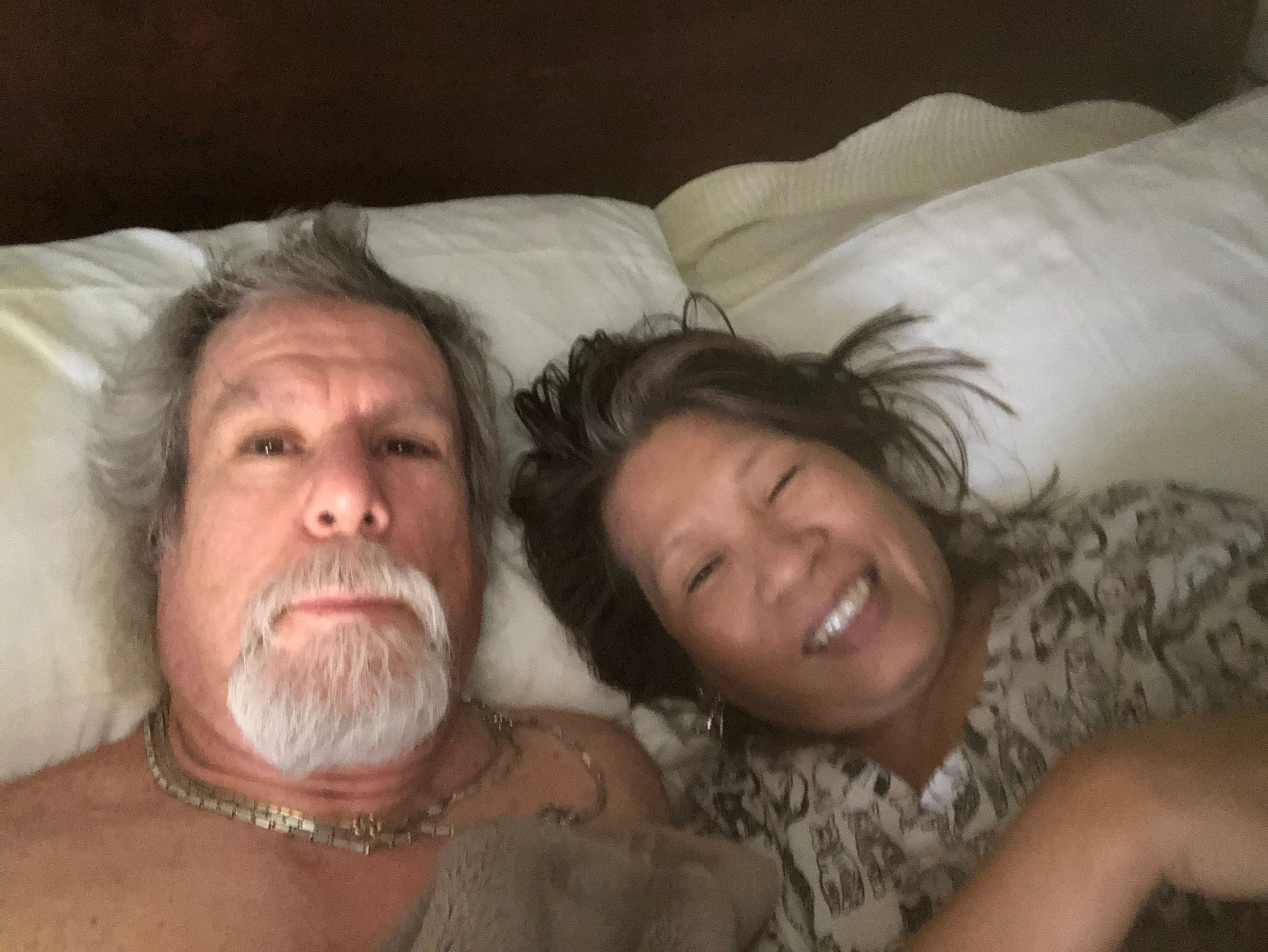 A couple lying in bed, smiling and relaxed.