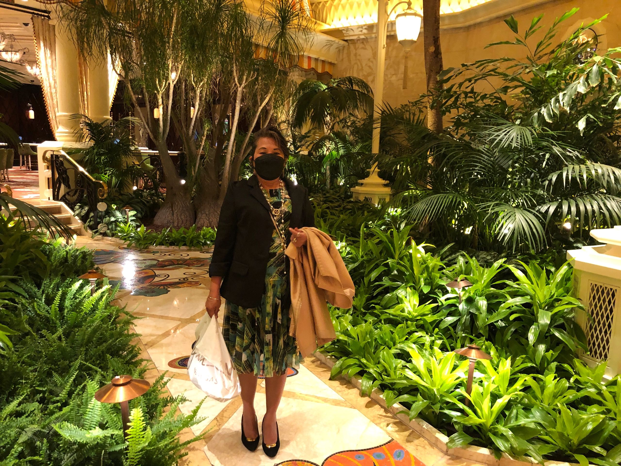 Woman wearing a mask standing in a lush indoor garden with elegant lighting.