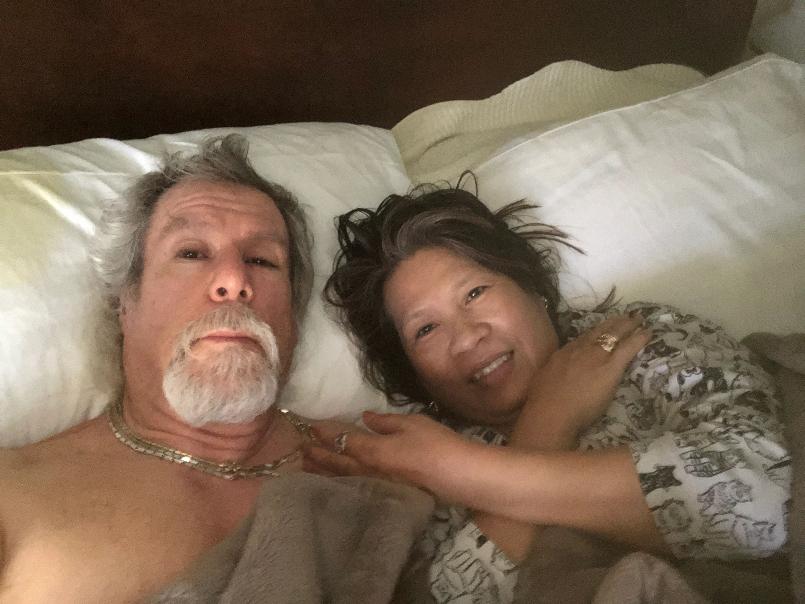 A couple lying in bed together, smiling at the camera.