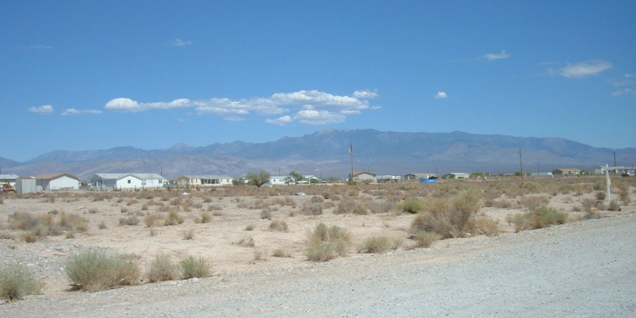 Dry desert landscape with sparse bushes and distant mountains under a clear blue sky.
