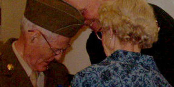 An elderly veteran and woman share a moment at an event.
