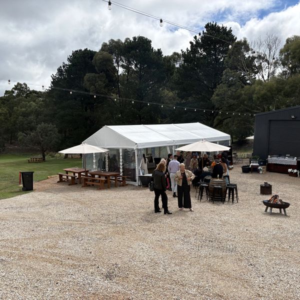 People gathered near a white event tent with outdoor seating and string lights.