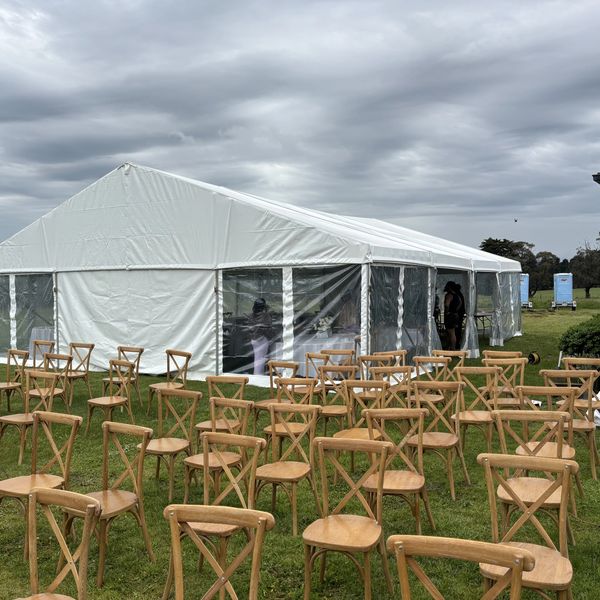 Wooden chairs arranged outside a large white event tent on a cloudy day.