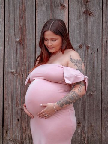 Pregnant woman in a pink dress tenderly holding her belly.
