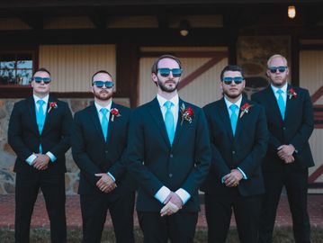 Five men in suits and sunglasses posing confidently outdoors.