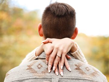 Woman's hands with an engagement ring hugging a man's neck outdoors.