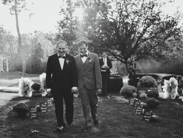 Two grooms holding hands and smiling at their outdoor wedding.