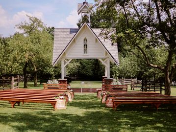Outdoor wedding setup with wooden benches and a small chapel.