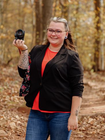 Smiling woman holding a camera in a forest during autumn.