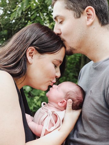 Parents lovingly kiss their newborn baby in a tender moment.